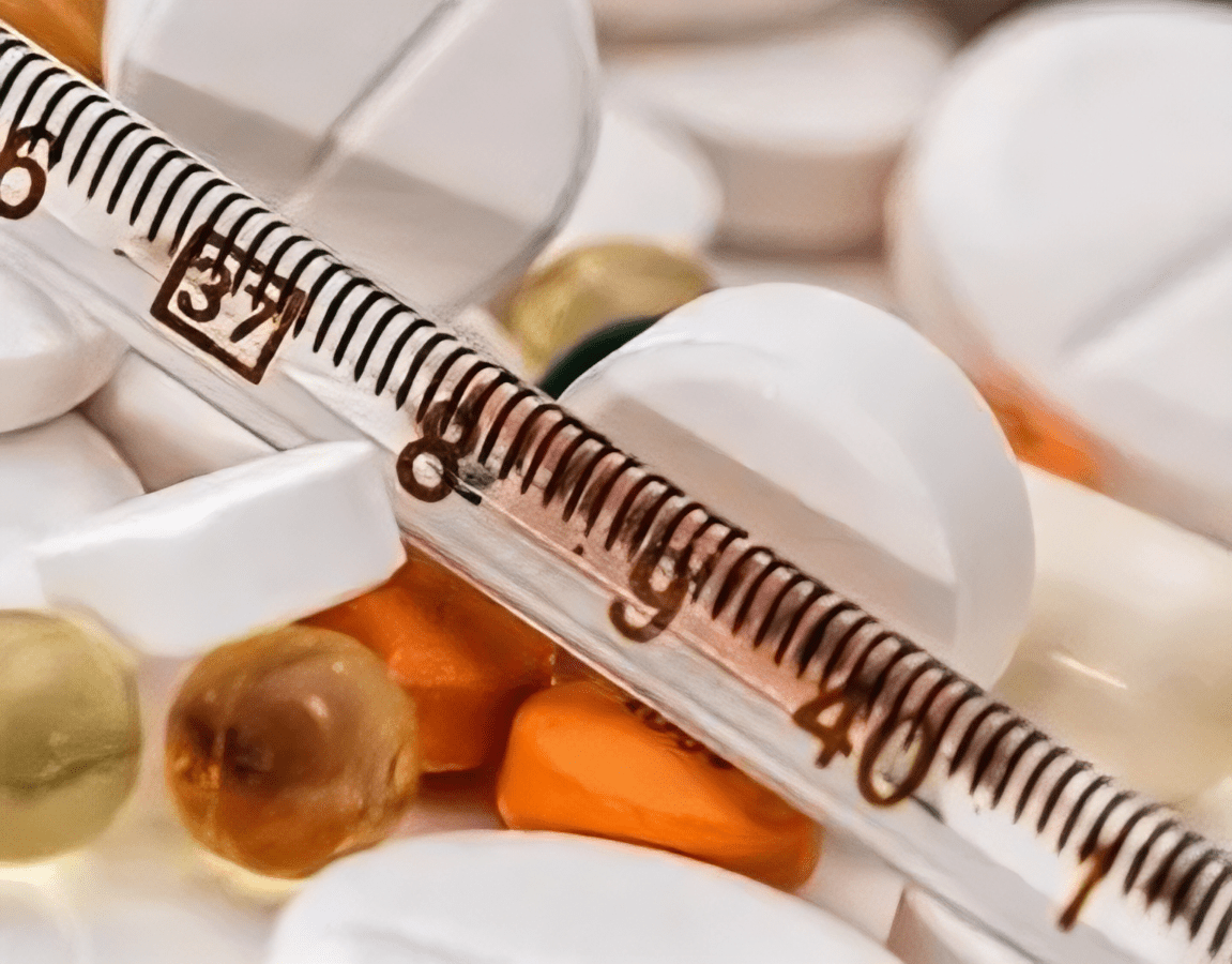close up image showing various pills and a thermometer emphasizing health and medicine
